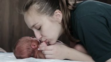 Genç, şefkatli bir anne, yeni doğmuş bebeğini öpüyor. Mutlu annelik anları, çocuk ve annelik bağı, ebeveynlik, çocuk bakımı kavramı.