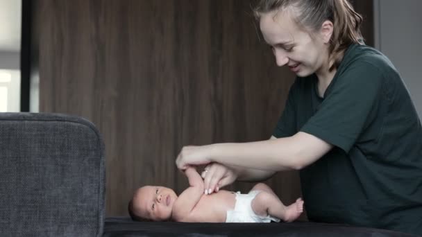 妈妈和一个新生婴儿一起做体操 这个婴儿躺在一个黑色的沙发上 — 图库视频影像