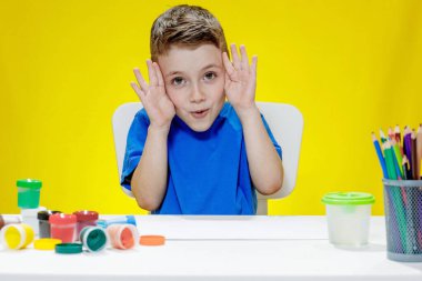 Avuç içleri gösteren mutlu küçük Avrupalı çocuk. Masada sarı arka planda boya çizmeye bayılıyor. Sanat ve fantezi, eğlence ve eğlence, öğrenme, rüyalar ve evde çocukluk.