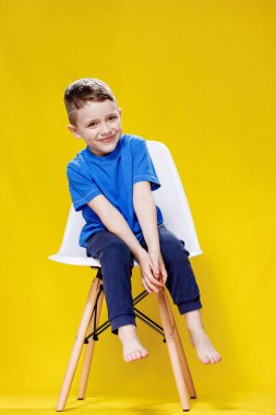 Sandalyeye oturan sıradan giysili pozitif çocuk..