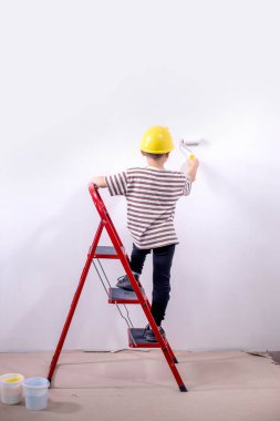 Bir çocuk müteahhit merdivenin üzerinde durur ve bir apartmanın beyaz duvarlarını boyar. Tadilat sırasında boya silindirli bir çocuk..