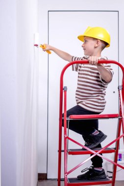 Boyalı silindirli şirin bir çocuk. Mutlu çocuk ebeveynlerin duvar boyamasına yardım eder. Aile için yeni bir ev