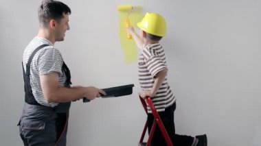 Baba ve oğlu evlerinin bir odasına sarı boyalı bir duvar boyuyorlar..