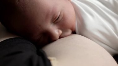 Yeni doğan bebeğe yakın çekim anne sütü emer. Güzel, huzurlu bir çocuk emzirirken huzur içinde uyuyor.