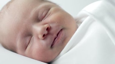 Beyaz bir örtüye sarılmış, beyaz bir arka planda uyuyan 3 günlük bir bebek..