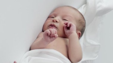 Yatakta uzanmış kollarını ve bacaklarını sallayan kameraya bakan mutlu yeni doğan bebeğin yan görüntüsü. Yeni doğan bebek konsepti.