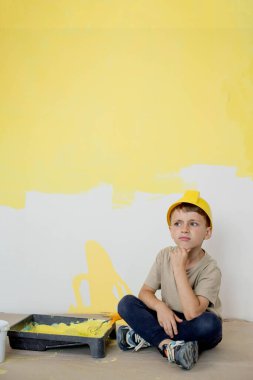 İnşaat üniformalı bir çocuk boyaların yanında oturuyor. Onarım. Duvarları boyuyorum..