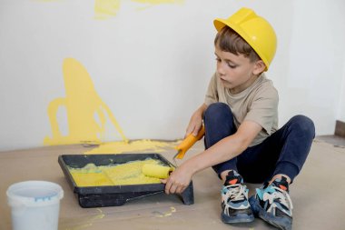 Ev tamiri. Boyalı silindirli şirin bir çocuk. Mutlu çocuk ebeveynlerin duvar boyamasına yardım eder. Yeni ev yenileme konsepti