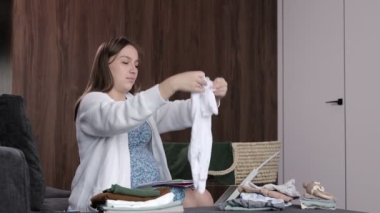 Hamile bir kadının çocuk kıyafetlerini katlayıp doğum hazırlığı için çantaya koyduğu bir video.