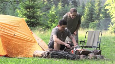 Piknikte çocuklu mutlu bir aile çadırın yanındaki ateşin yanında oturur ve ormanda kamp ateşinde yemek pişirir. Kamp, dinlenme, yürüyüş..