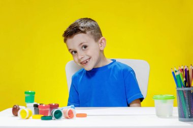 Masada boyaları ve renkli kalemleri olan gülümseyen bir çocuğun portresi. Yaratıcı sanat gelişimi ve çocuk eğlencesi.