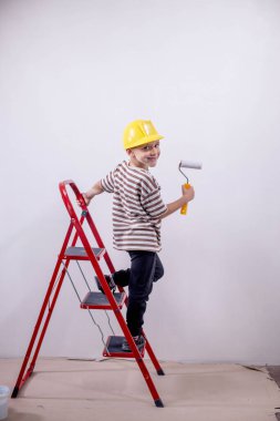 Bir çocuk müteahhit merdivenin üzerinde durur ve bir apartmanın beyaz duvarlarını boyar. Tadilat sırasında boya silindirli bir çocuk..
