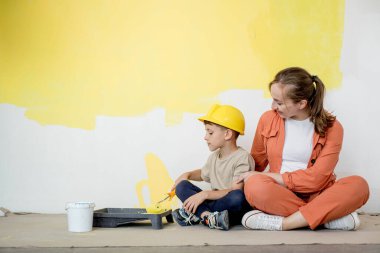 Ev tamiri. Anne oğluna bir silindirle duvarı boyamasında yardım ediyor. Çocuk dairenin duvarını boyuyor. Yeni ev yenileme konsepti
