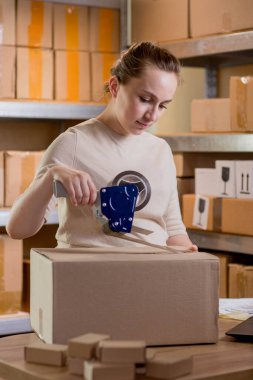 Gülümseyen bayan girişimci bant kutusunu kullanarak paketliyor. Kadın, ürün kutusunu müşteriye teslim etmek için hazırlıyor. Çevrimiçi iş, ekommerce ve dağıtım kavramı.