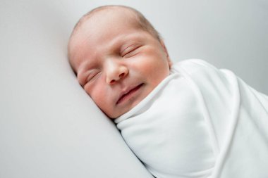 Beyaz bir örtüye sarılmış, beyaz bir arka planda uyuyan 3 günlük bir bebek..