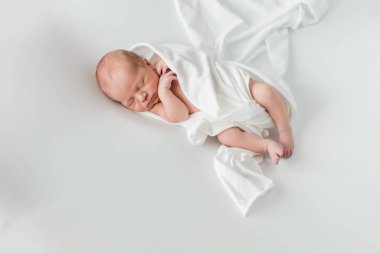 Beyaz bir örtüye sarılmış, beyaz bir arka planda uyuyan 3 günlük bir bebek..