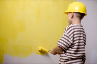 Boyalı silindirli şirin bir çocuk. Mutlu çocuk ebeveynlerin duvar boyamasına yardım eder. Ev yenilenmesi.