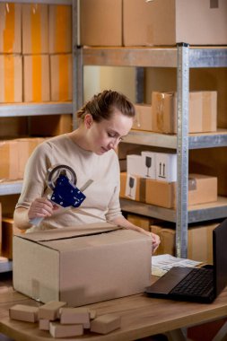 Gülümseyen bayan girişimci bant kutusunu kullanarak paketliyor. Kadın, ürün kutusunu müşteriye teslim etmek için hazırlıyor. Çevrimiçi iş, ekommerce ve dağıtım kavramı.