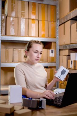 Paket bilgilerini hazırlarken elinde bir kutu tutan ve klavyeye bir şey yazan bir iş kadını portresi. Posta hizmeti ve küçük işletme kavramı.