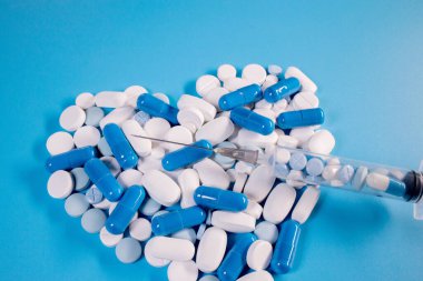 Kalp şeklinde haplar ve mavi arka planda bir şırınga. Kalp sağlığı için ilaçlar. Tıp ve sağlık hizmetleri kavramı.