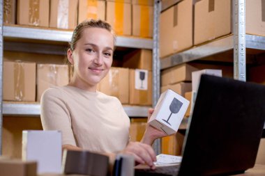 Paket bilgilerini hazırlarken elinde bir kutu tutan ve klavyeye bir şey yazan bir iş kadını portresi. Posta hizmeti ve küçük işletme kavramı.