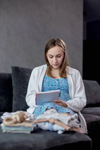 Pregnant woman packing bag for maternity hospital, making notes, checking list in diary. Expectant mother with suitcase of baby clothes and necessities preparing for newborn birth during pregnancy