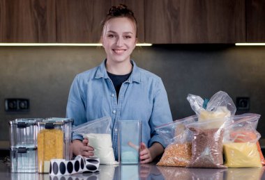 Konforlu ürün deposu için plastik kutularla poz veren mutlu kadın profesyonel uzay organizatörü. Organizasyonun modern bir mutfağın içinde yönetimi..