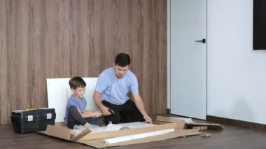 Baba ve oğul yeni dairenin zemininde yeni mobilyalar birleştiriyor. Tecrübe ve eğitim kavramı..