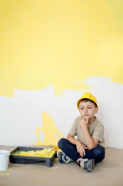 İnşaat üniformalı bir çocuk boyaların yanında oturuyor. Onarım. Duvarları boyuyorum..