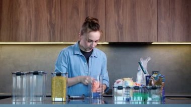 Kadın mutfaktaki depoyu düzenlemek için plastik kutu kullanıyor. Gıda ürünlerinin tasarımı ve sıralanması