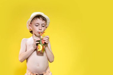 Sarı arka planda şişme yüzük ve kokteyl bardağı olan şirin bir çocuk..