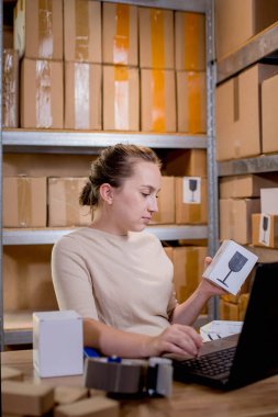 Paket bilgilerini hazırlarken elinde bir kutu tutan ve klavyeye bir şey yazan bir iş kadını portresi. Posta hizmeti ve küçük işletme kavramı.