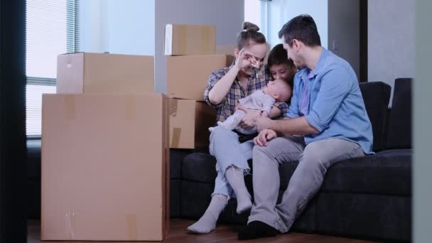 新しい家に引っ越す家族 新しく購入したアパートの箱の近くに座っている子供たちと幸せで興奮する両親 — ストック動画
