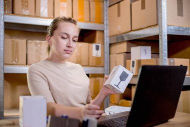 Paket bilgilerini hazırlarken elinde bir kutu tutan ve klavyeye bir şey yazan bir iş kadını portresi. Posta hizmeti ve küçük işletme kavramı.