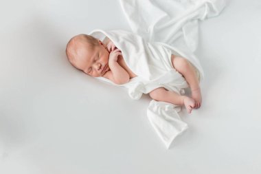 Beyaz bir örtüye sarılmış, beyaz bir arka planda uyuyan 3 günlük bir bebek..