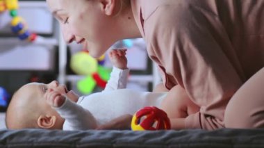 Genç anne sırt üstü yatarken bebeğiyle konuşur ve onunla oynar. Bebek bakımı, annelik kavramı.