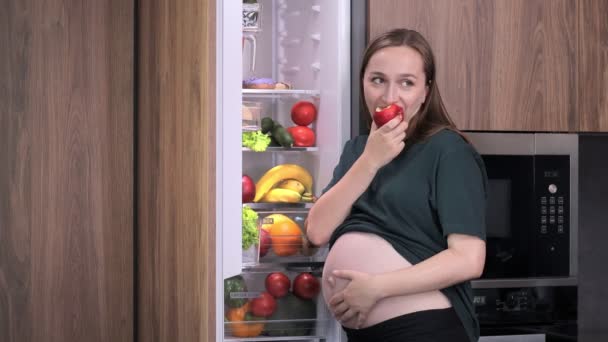 自宅で冷蔵庫の近くにリンゴを持っている若い妊婦 — ストック動画