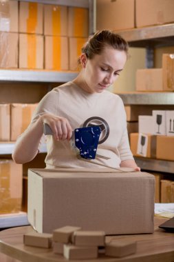 Gülümseyen bayan girişimci bant kutusunu kullanarak paketliyor. Kadın, ürün kutusunu müşteriye teslim etmek için hazırlıyor. Çevrimiçi iş, ekommerce ve dağıtım kavramı.