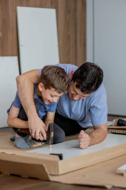 Baba ve oğul yeni dairenin zemininde yeni mobilyalar birleştiriyor. Tecrübe ve eğitim kavramı.