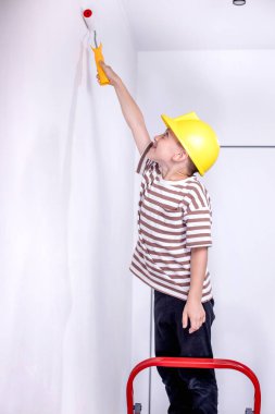 Boyalı silindirli şirin bir çocuk. Mutlu çocuk ebeveynlerin duvar boyamasına yardım eder. Aile için yeni bir ev