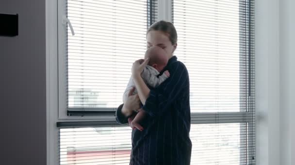 一位漂亮的年轻女子站在窗边抱着孩子 可爱的小家伙在他母亲的怀抱中休息 — 图库视频影像
