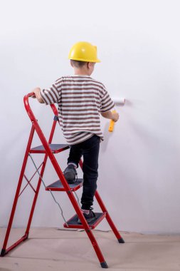 Bir çocuk müteahhit merdivenin üzerinde durur ve bir apartmanın beyaz duvarlarını boyar. Tadilat sırasında boya silindirli bir çocuk..