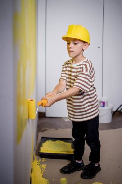 Boyalı silindirli şirin bir çocuk. Mutlu çocuk ebeveynlerin duvar boyamasına yardım eder. Ev yenilenmesi.