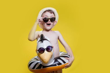 Yaz panamalı çocuk ve sarı arka planda şişirilebilir yüzme çemberi olan güneş gözlüklü..