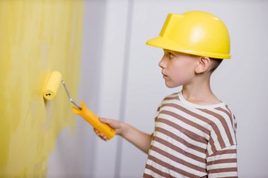 Boyalı silindirli şirin bir çocuk. Mutlu çocuk ebeveynlerin duvar boyamasına yardım eder. Aile için yeni bir ev