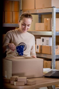 Gülümseyen bayan girişimci bant kutusunu kullanarak paketliyor. Kadın, ürün kutusunu müşteriye teslim etmek için hazırlıyor. Çevrimiçi iş, ekommerce ve dağıtım kavramı.