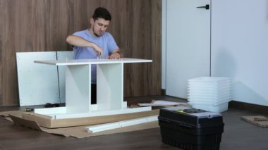 Genç adam, tahta bir mobilya yüzeyine büyü anahtarıyla çelik bir cıvata vidalıyor. Kendini toparla.