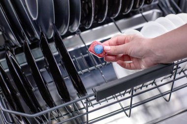 Açık bir bulaşık makinesinin arka planına karşı bir kadının ellerinde bulaşık makinesi tableti..