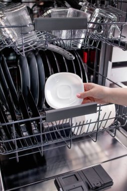 Kadın bulaşık makinesine bir tabak koyar ya da ondan alır. Genç Ev Kadınları Evi Temiz Tutmak İçin Modern Aletler Kullanıyor.