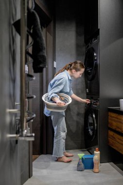 Kadın otomatik çamaşır makinesini açar ya da banyodaki kontrol paneli düğmeli programı, evdeki modern aletleri seçer..